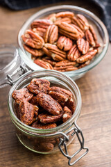 Pecan nuts coated in sugar and honey in jar on wooden table.