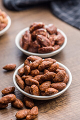 Almond nuts coated in sugar and honey in bowl on wooden table.