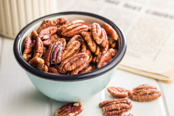 Peeled pecan nuts in bowl on white table.