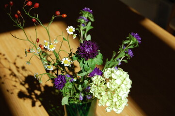 テーブルの上の緑色の花瓶に生けられた白い花と紫の花と赤い実とそれの影