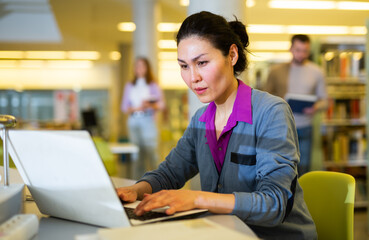 Asian woman student studying at the university by correspondence studies in the library on a laptop...