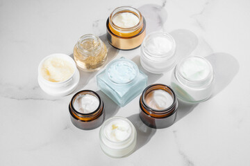 Cosmetics packaging. Set of different cosmetic jars of face cream, mask, balm on beigemarble background. Blank packaging. Natural beauty spa product concept. Beauty Mock-up