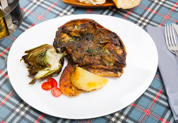 Delicious baked head of lamb served on white plate with roasted potatoes and artichoke