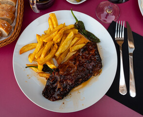 Hearty satisfying dish of succulent barbecue ribs with crispy golden french fries and roasted jalapeno peppers accompanied by pickled olives and red wine
