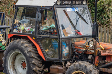 A tractor with a cabin full of junk stands in the yard of a family farm