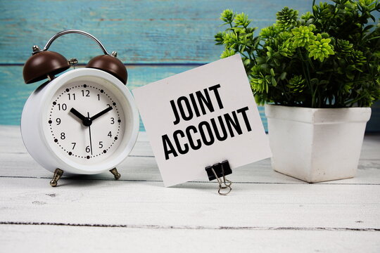 Joint Account text written on paper card with alarm clock on wooden background
