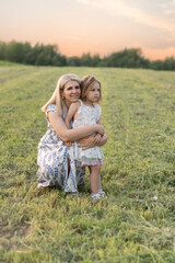 Mom hugs her daughter, they admire the beautiful summer weather. A happy family, mother and daughter in the rays of the sun against the sky. The concept of a happy family, girls, childhood.