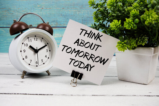 Naklejki Think about tomorrow today  text written on paper card with alarm clock on wooden background