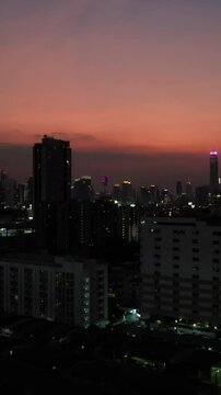  vertical video, night illumination of center ofBangkok at sunset with orange sky and dark buildings