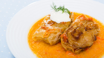 Homemade cabbage rolls in leaves of cabbage at plate with sour cream and greens