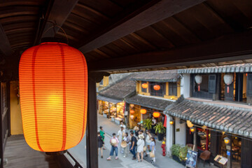 An illuminated red paper lantern hang on balcony over Asian street with traditional architecture
