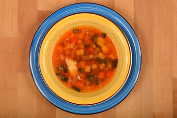 A top-down shot of a yellow bowl of clear vegetable soup with semolina dumplings and various...
