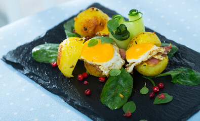 Burgers with potato, bacon slices and fried quail eggs garnished with salad leaves and cucumbers