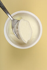 A close-up, overhead shot captures a spoonful of thick white yogurt being lifted from a white container against a plain background