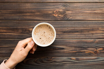 Minimalistic style woman hand holding a cup of coffee on Colored background. Flat lay, top view cappuccino cup. Empty place for text, copy space. Coffee addiction. Top view, flat lay