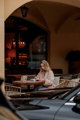 A young Caucasian woman with blonde hair sits at a cafe table in Saint Petersburg, reading a book....