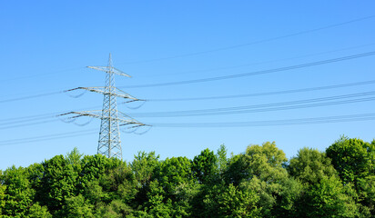 Obraz premium Transmission tower with clear blue sky in sunny summer weather - high voltage electricity over green trees of dense healthy forest landscape - concept of distribution, energy infrastructure - Germany