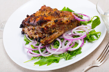 Image of tasty pork ribs baked under sauce, served with arugula and onion salad