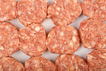 A close-up, overhead shot shows a group of raw savory minced meat and cheese patties filling the frame, displaying their texture