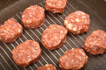 A close-up, overhead shot shows raw savory minced meat and cheese patties arranged on a dark grill pan, ready for cooking
