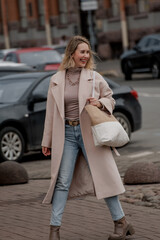 Obraz premium A young Caucasian woman with long blonde hair walks briskly across a street in Saint Petersburg. She wears a light coat and carries a large bag.