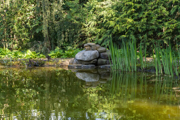 Tranquil pond with stacked rocks and lush greenery, reflecting serene natural beauty. Nature concept for spring design.