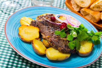 Tasty beef steak with baked potatoes served at plate with greens