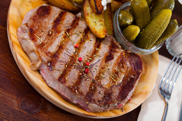 Spicy medium rare roasted veal steak with fried potato wedges with sauce and pickles on wooden board