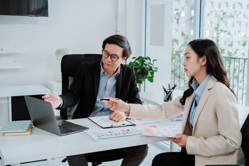 Two asian business colleagues working together in office. Business team brainstorming, having a discussion about work project, working on laptop computer at modern office. Business teamwork