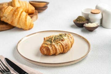 Herb-topped croissant on a plate in a cozy breakfast setting.