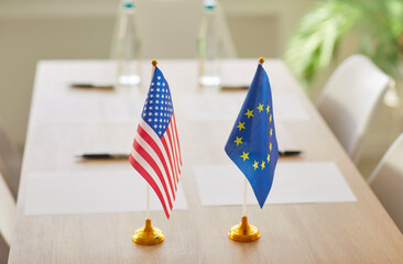 Flags of United States and European Union standing on wooden table on international negotiations for conclusion of contracts between countries. Unity and global partnership concept.