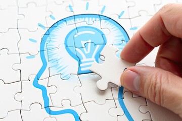 Hand Fitting Puzzle Piece to Complete Idea Lightbulb on White Jigsaw