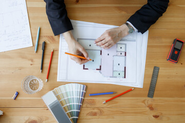 Architect reviews floor plan design at workspace on wooden table with various tools and materials