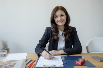 Professional woman working at a desk, smiling while taking notes during a business meeting or planning session
