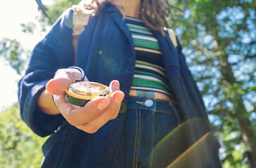 Woman Holds a Compass in Her Hand, Surrounded by Green Trees in a Sunny Outdoor Setting.