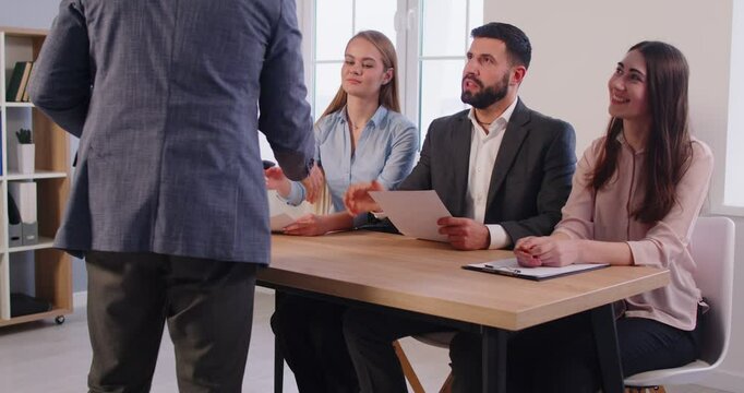 Confident male job applicant shaking hands with group of recruiters before interview in office. Panel of smiling HR managers greeting candidate with handshake, conducting hiring process in workplace.
