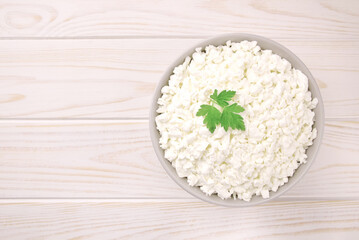 Farm cheese in a bowl on a light wooden background. Cottage cheese with parsley.
