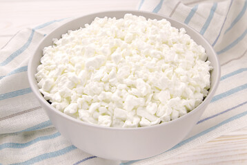 Farm cheese in a bowl on a light wooden background.