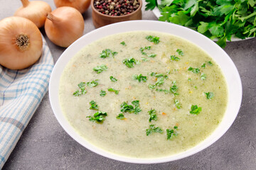 Homemade cream soup with chicken and herbs in a white plate on a gray background.