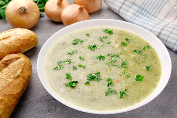 Homemade cream soup with chicken and herbs in a white plate on a gray background.