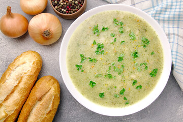 Homemade cream soup with chicken and herbs in a white plate on a gray background.