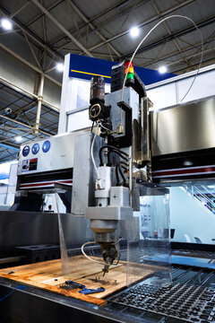 High-tech waterjet cutting machine head processing material on a production bed with safety guards and industrial signals, showcasing modern industrial manufacturing equipment.