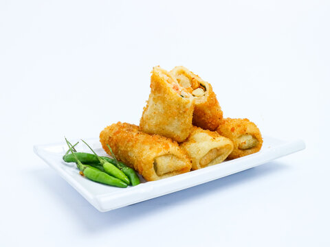 Indonesian risoles filled with vegetables, served with fresh green chilies on a white plate. Crispy breadcrumb coating on white background