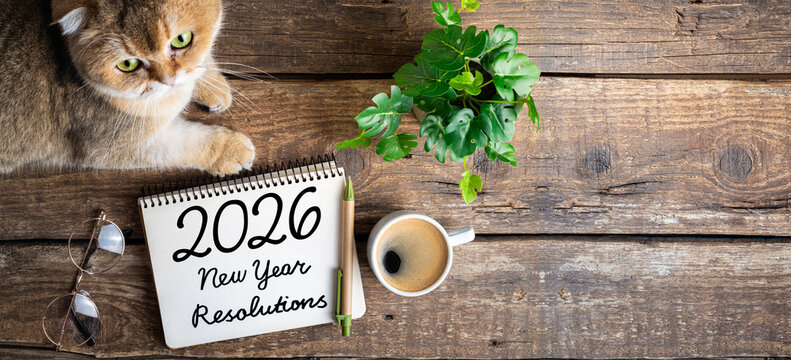 New year resolutions 2026 on desk. 2026 resolutions list with notebook, coffee cup, cute cat on table. Goals, resolutions, plan, cozy, hygge concept. New Year 2026 background, copy space