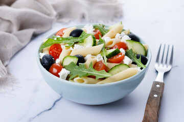 Mediterranean Pasta Salad in bowl with Fresh Vegetables and Herbs on white marble background