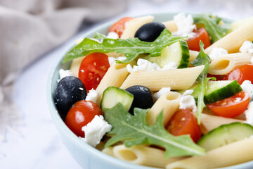 Mediterranean Pasta Salad in bowl with Fresh Vegetables and Herbs on white marble background