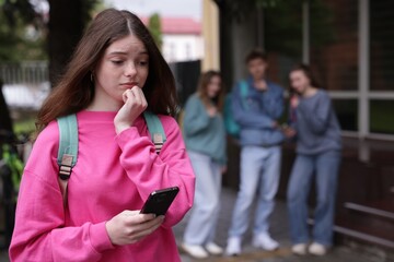 Teenage girl with smartphone suffering from bullying at school, selective focus