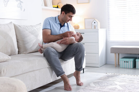 Father feeding his little baby with bottle on sofa at home - Powered by Adobe