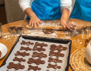 Close-up of child in apron kneading chocolate cookie dough on a messy wooden table with flour. Homemade baking process and hands-on kitchen learning