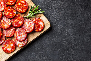Fresh chorizo slices beautifully arranged on a wooden board with a sprig of rosemary garnish.
